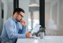 Unternehmer sitzt an einem Tisch im Büro vor Laptop und liest