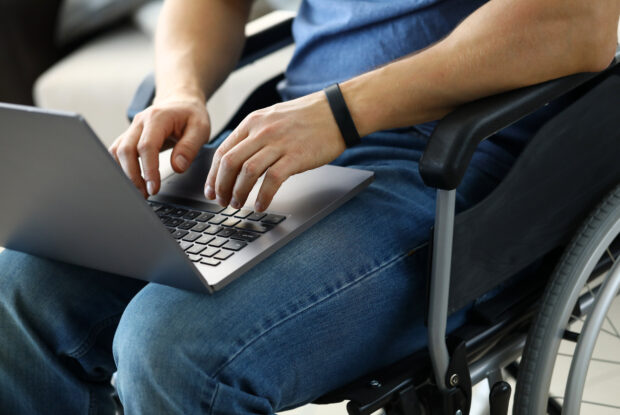 Mann sitzt im Rollstuhl und arbeitet am Laptop